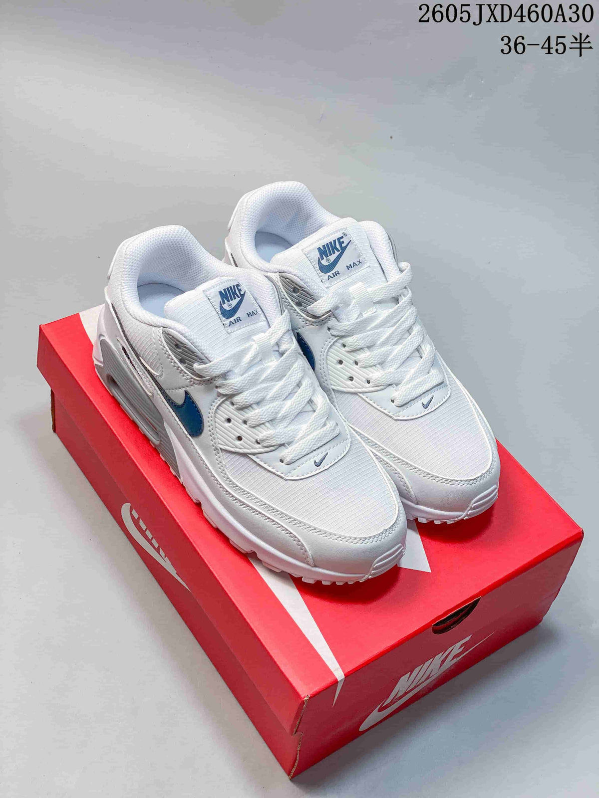 Pair of white Nike Air Max 90 sneakers with blue accents on a red shoe box