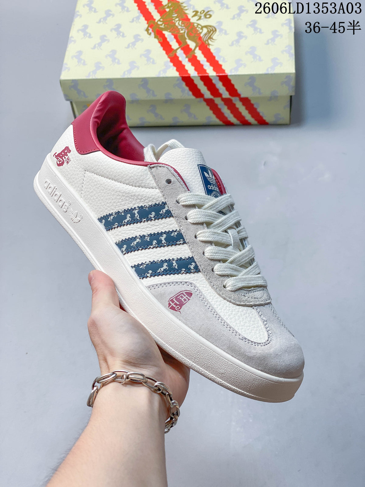 White Gazelle Indoor sneaker with blue patterned stripes, gray suede-look panels, and pink collar accents.