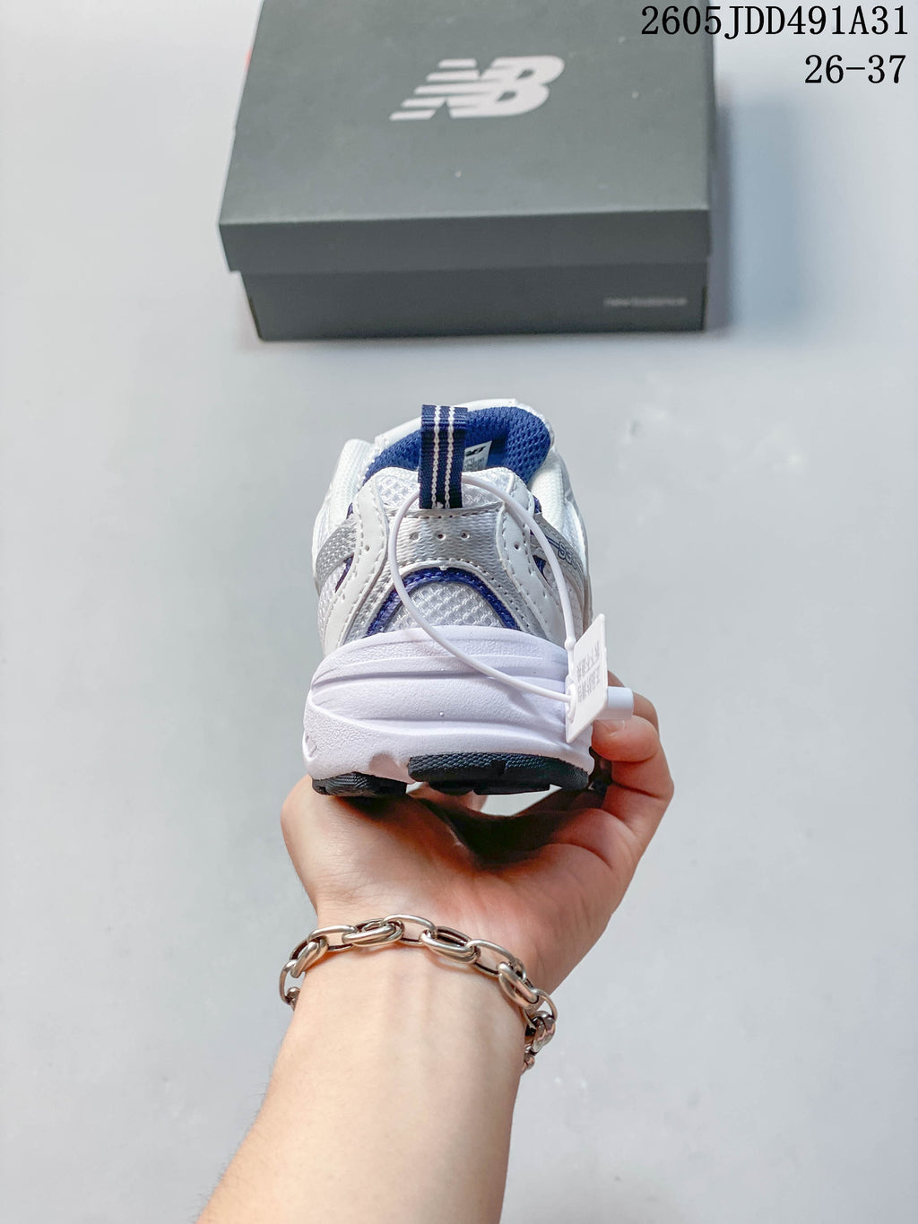 Rear view of a white and navy New Balance kids' sneaker, showing the heel and pull tab.