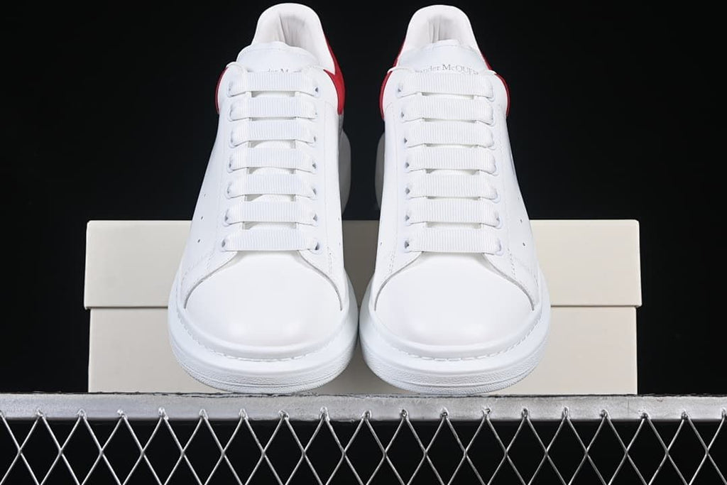 Front view of the pair of white sneakers with broad laces and red heel accents.