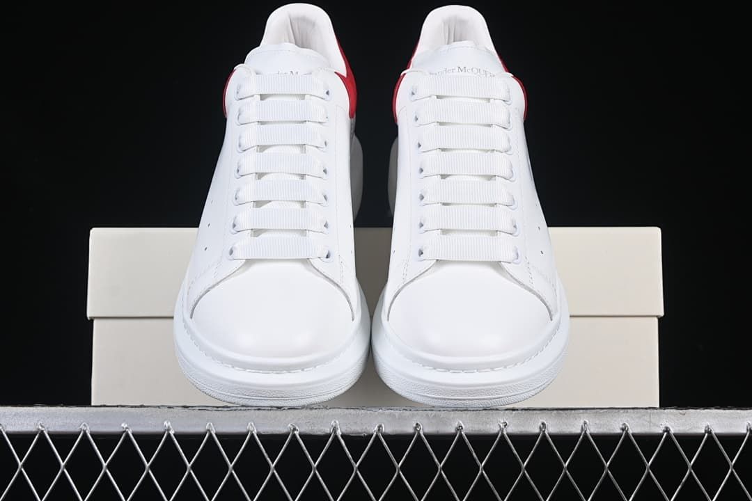 Front view of the pair of white sneakers with broad laces and red heel accents.