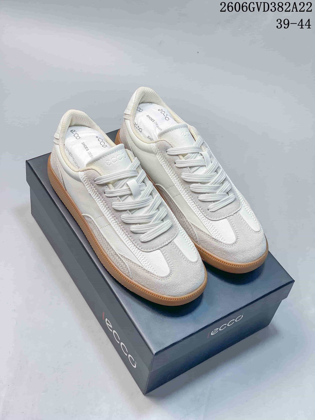Off-white ECCO low-top lace-up sneakers with contrast panels and gum-colored soles, shown on a shoe box.