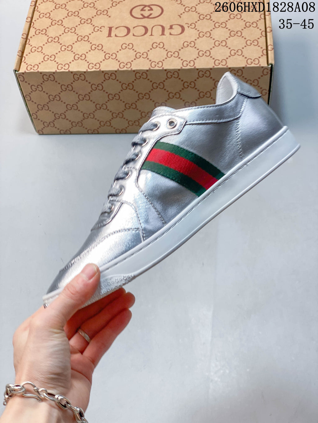 Side view of a silver lace-up sneaker with a green-and-red stripe and white sole.