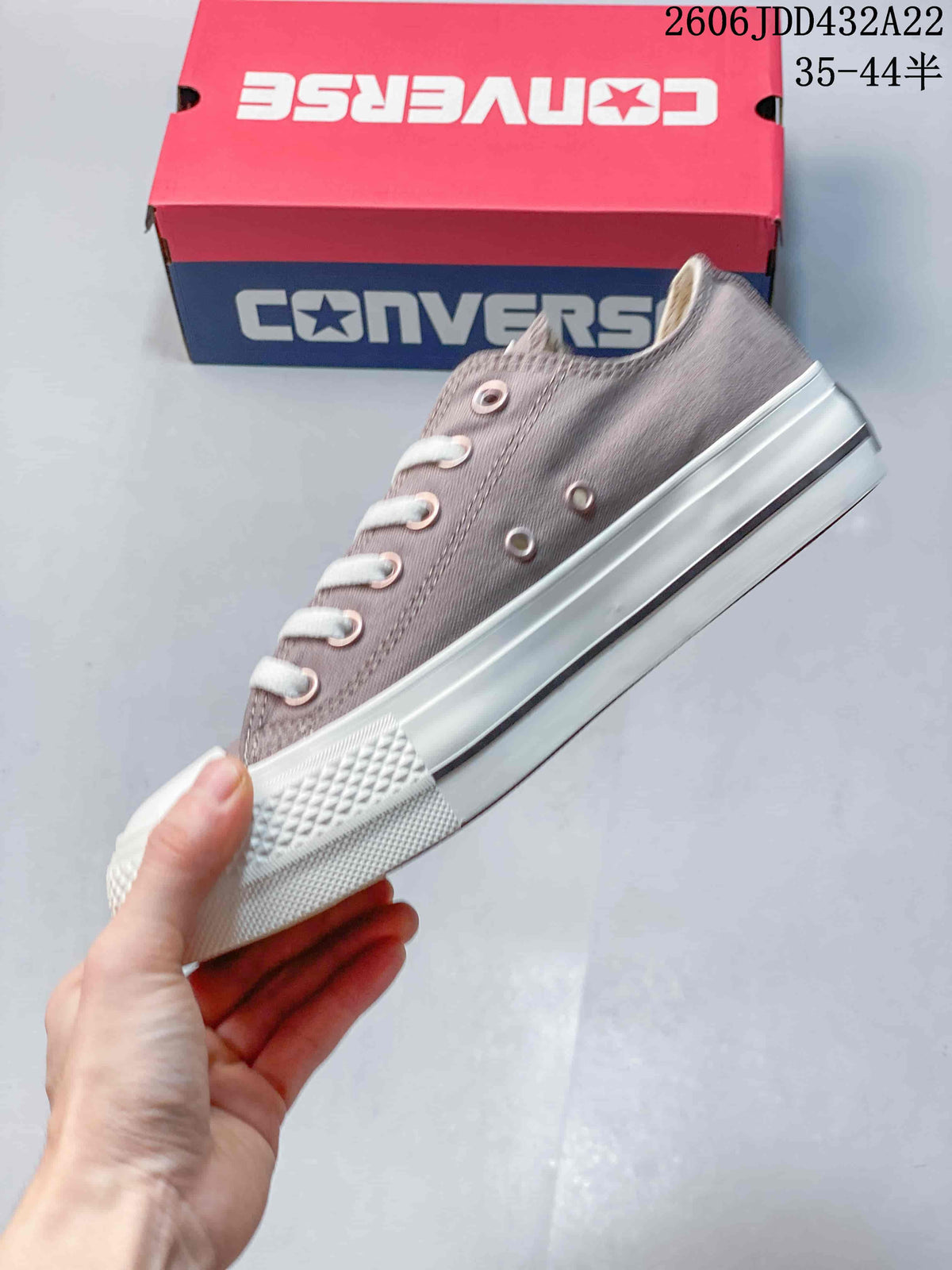 Side view of a taupe low-top Converse sneaker showing its white sole and dark stripe