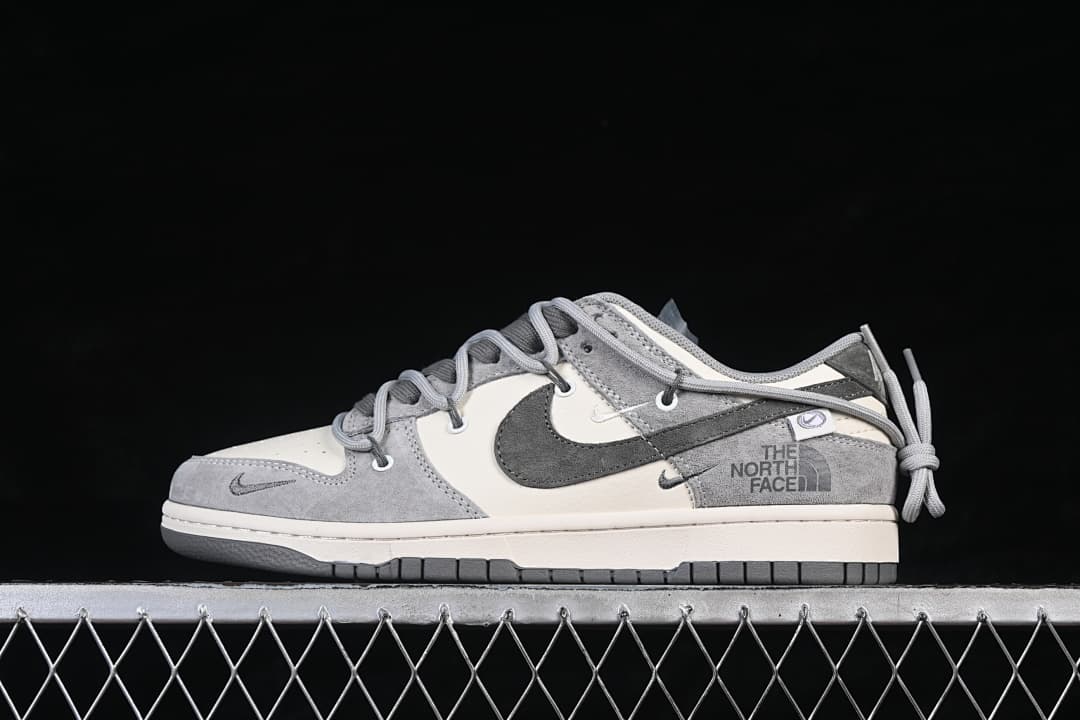 Side profile of a grey and off-white low-top sneaker with a large Swoosh, The North Face graphics, and heel lace details.