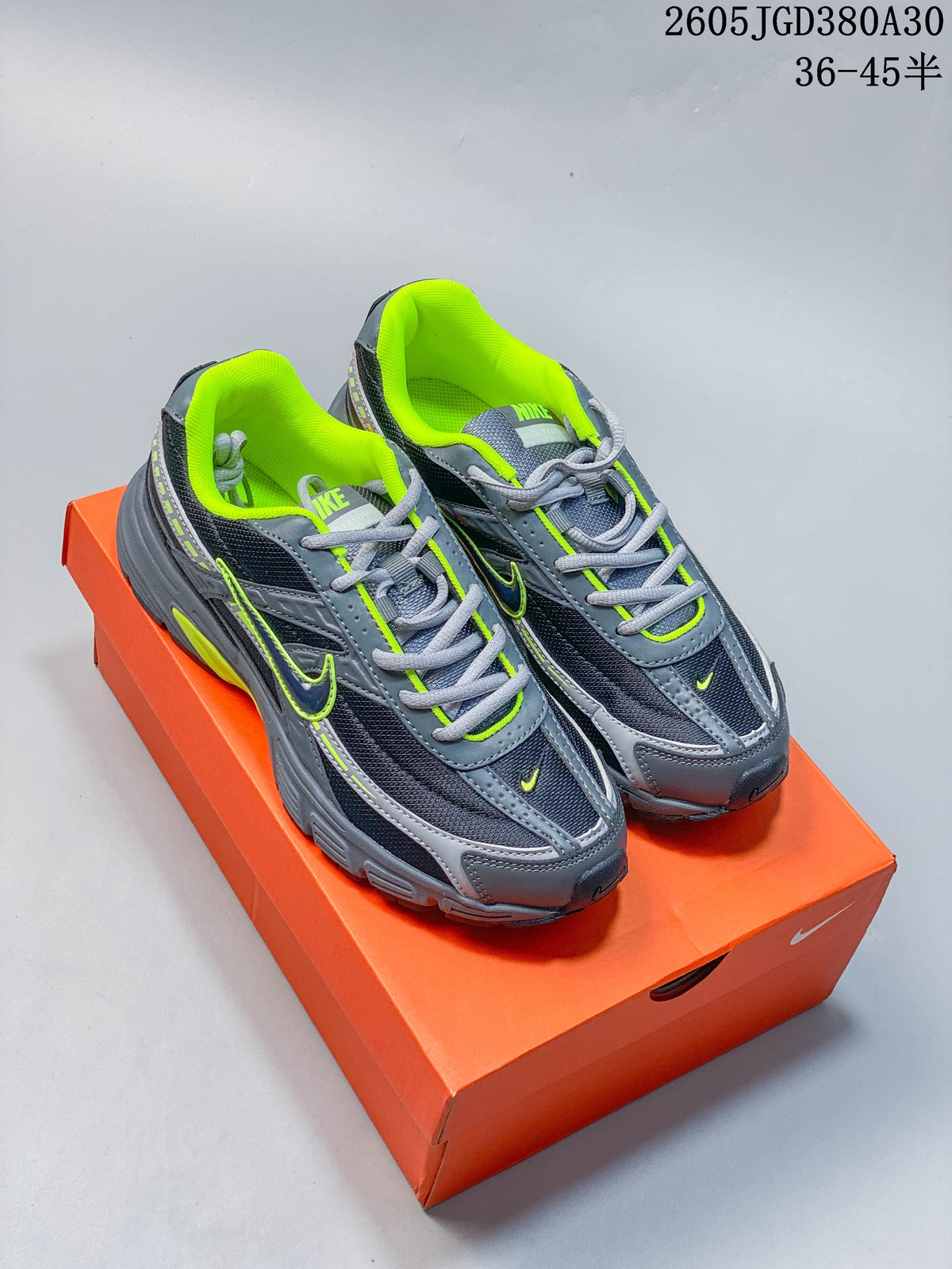 Pair of gray and dark navy Nike running-style sneakers with volt green accents, shown on an orange shoe box.