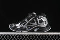 Side profile of a black and silver Balenciaga Runner-style sneaker against a dark background.