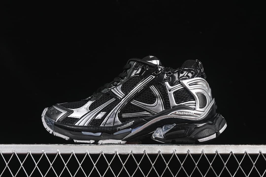 Side profile of a black and silver Balenciaga Runner-style sneaker against a dark background.