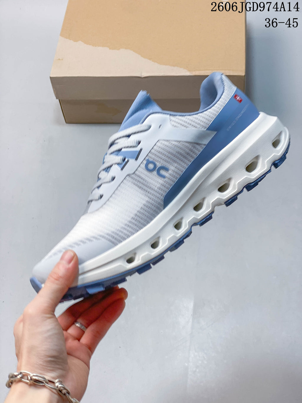 Side view showing the patterned upper and sculpted outsole of a white and blue On Cloudvista 2 shoe