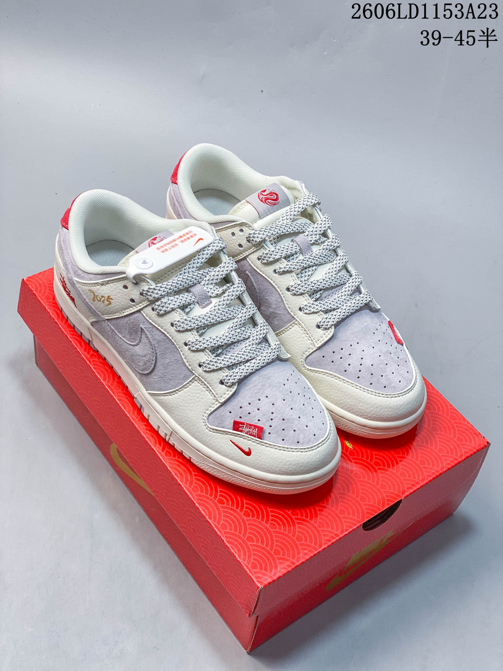 Pair of light gray and off-white low-top sneakers with red accents on a red patterned box