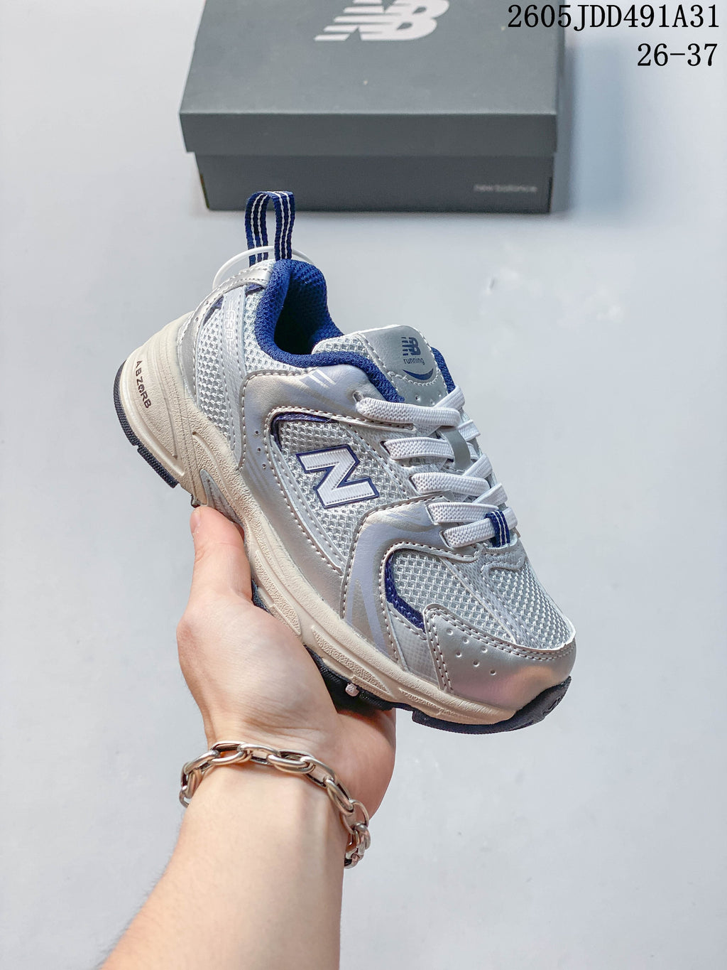 Silver-toned kids' New Balance 530 lace-up sneaker with blue accents, shown in hand.