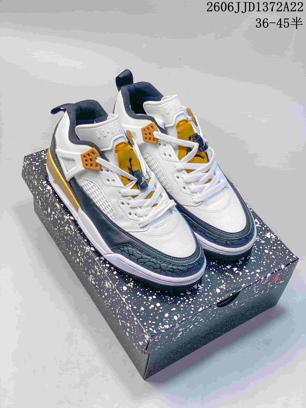 White Jordan Spizike Low sneakers with dark blue-gray and mustard accents on a speckled box