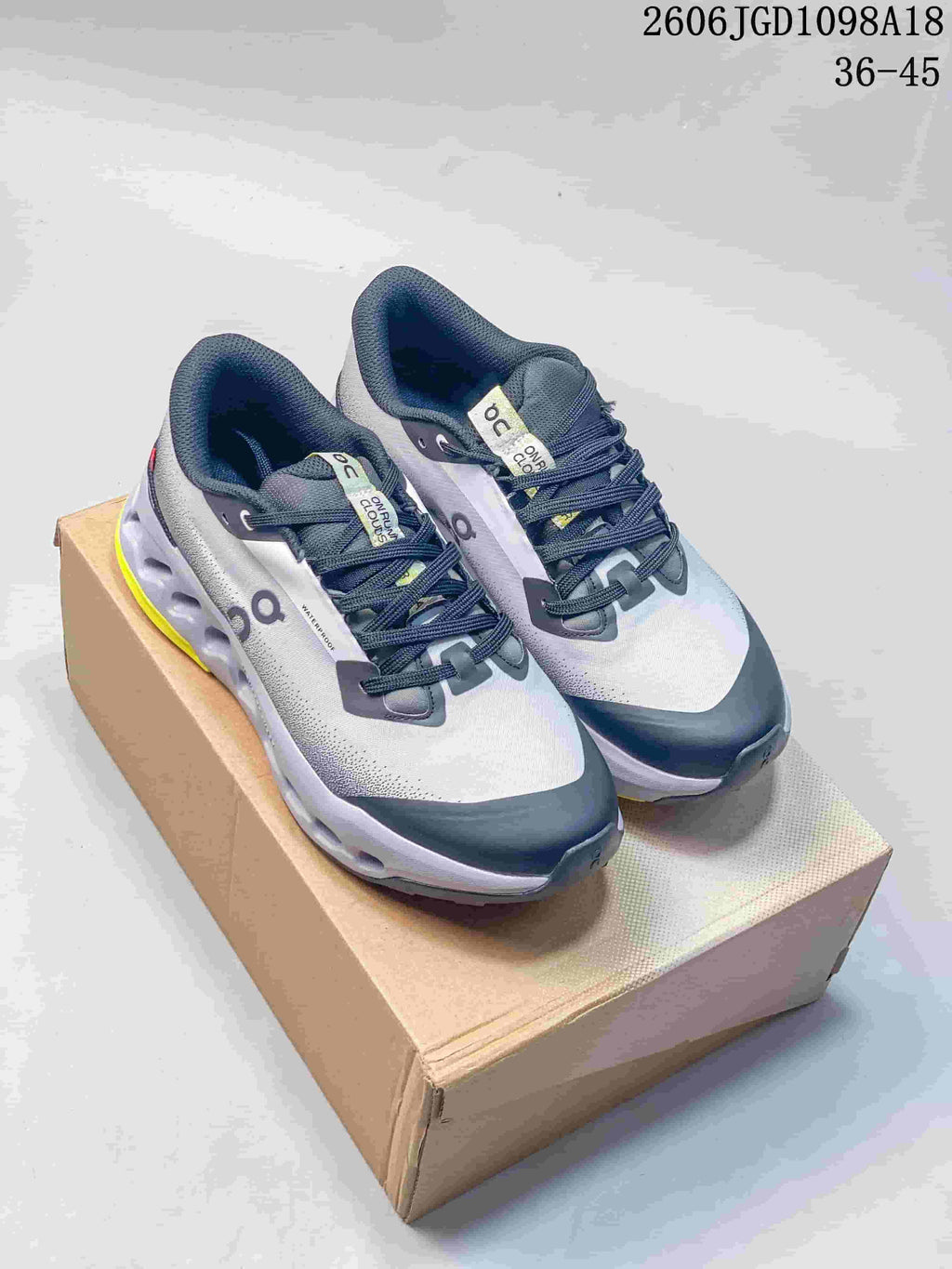 Pair of gray and navy On Cloudmonster 3 shoes with yellow outsole accents, shown on a box
