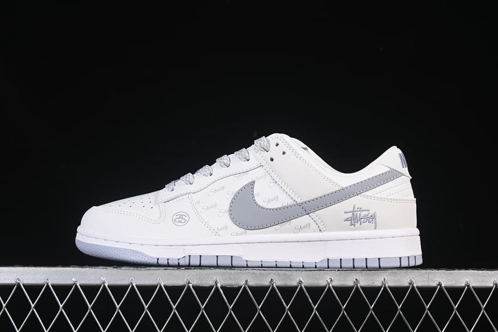 Side view of a white low-top Nike SB Dunk with a grey Swoosh, grey laces, repeated script print and heel graphic.