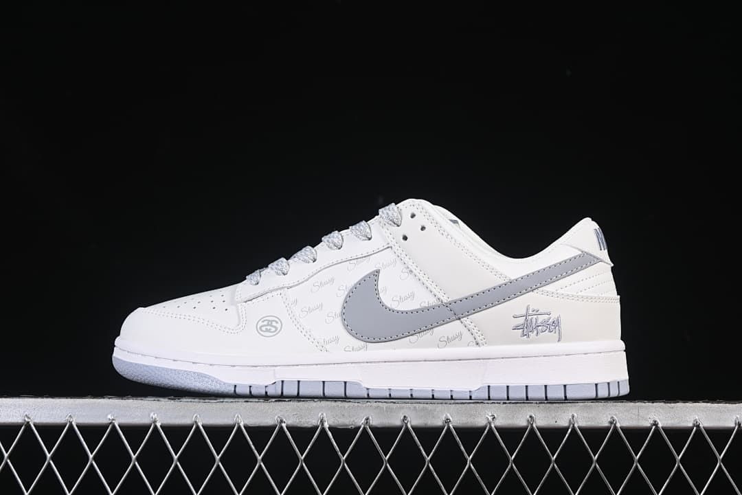 Side view of a white low-top Nike SB Dunk with a grey Swoosh, grey laces, repeated script print and heel graphic.