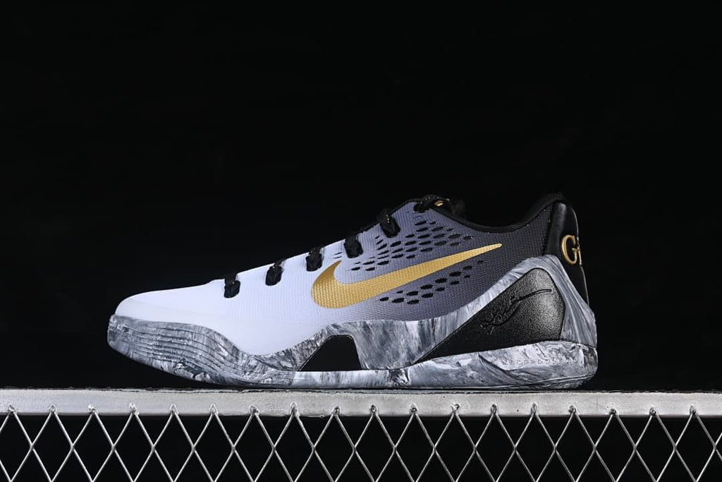 Side view of a white, gray, black, and gold low-top Kobe basketball shoe