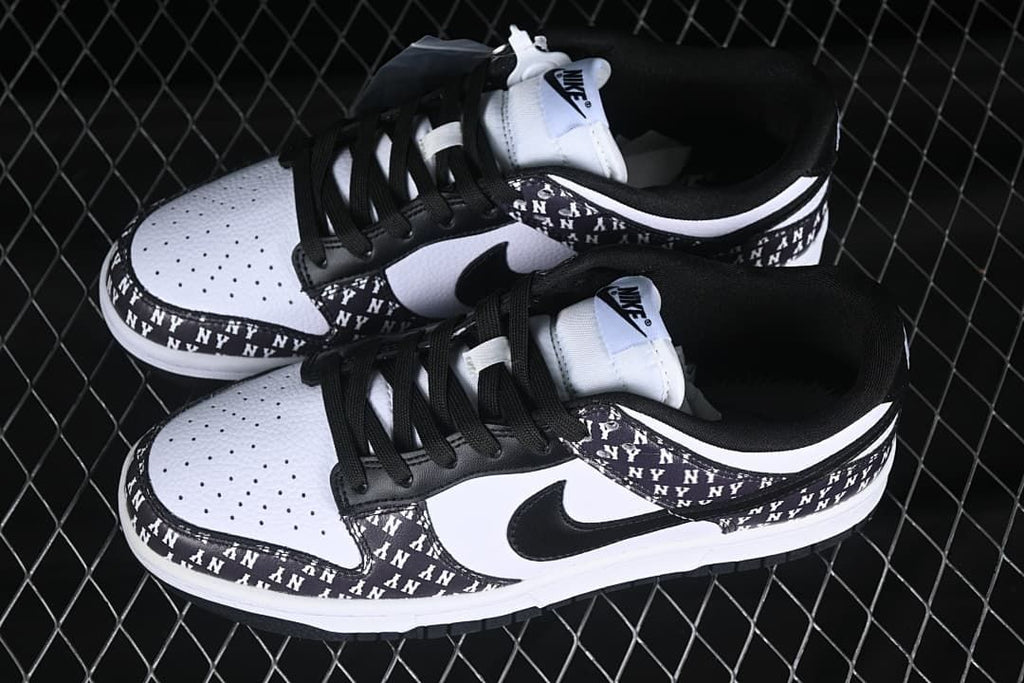 Pair of black-and-white Nike SB Dunk Low sneakers showing perforated toe panels, black laces, and NY-print overlays.