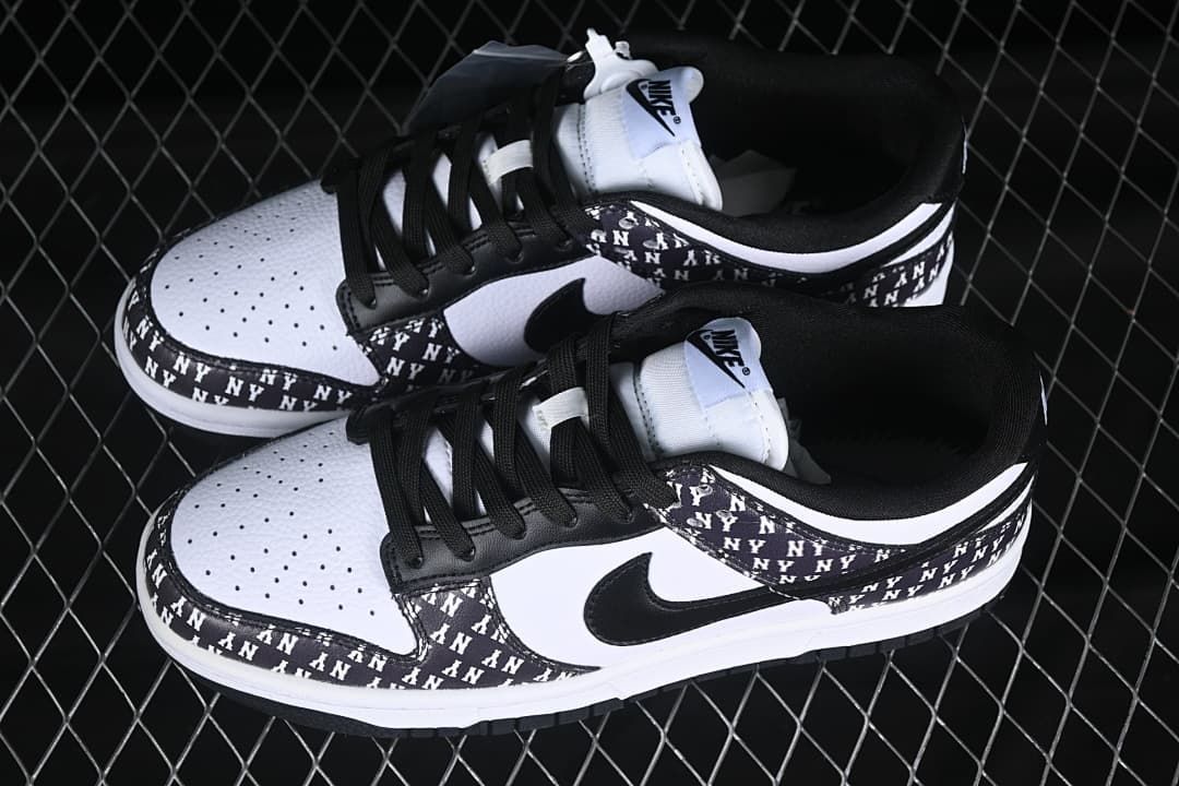 Pair of black-and-white Nike SB Dunk Low sneakers showing perforated toe panels, black laces, and NY-print overlays.