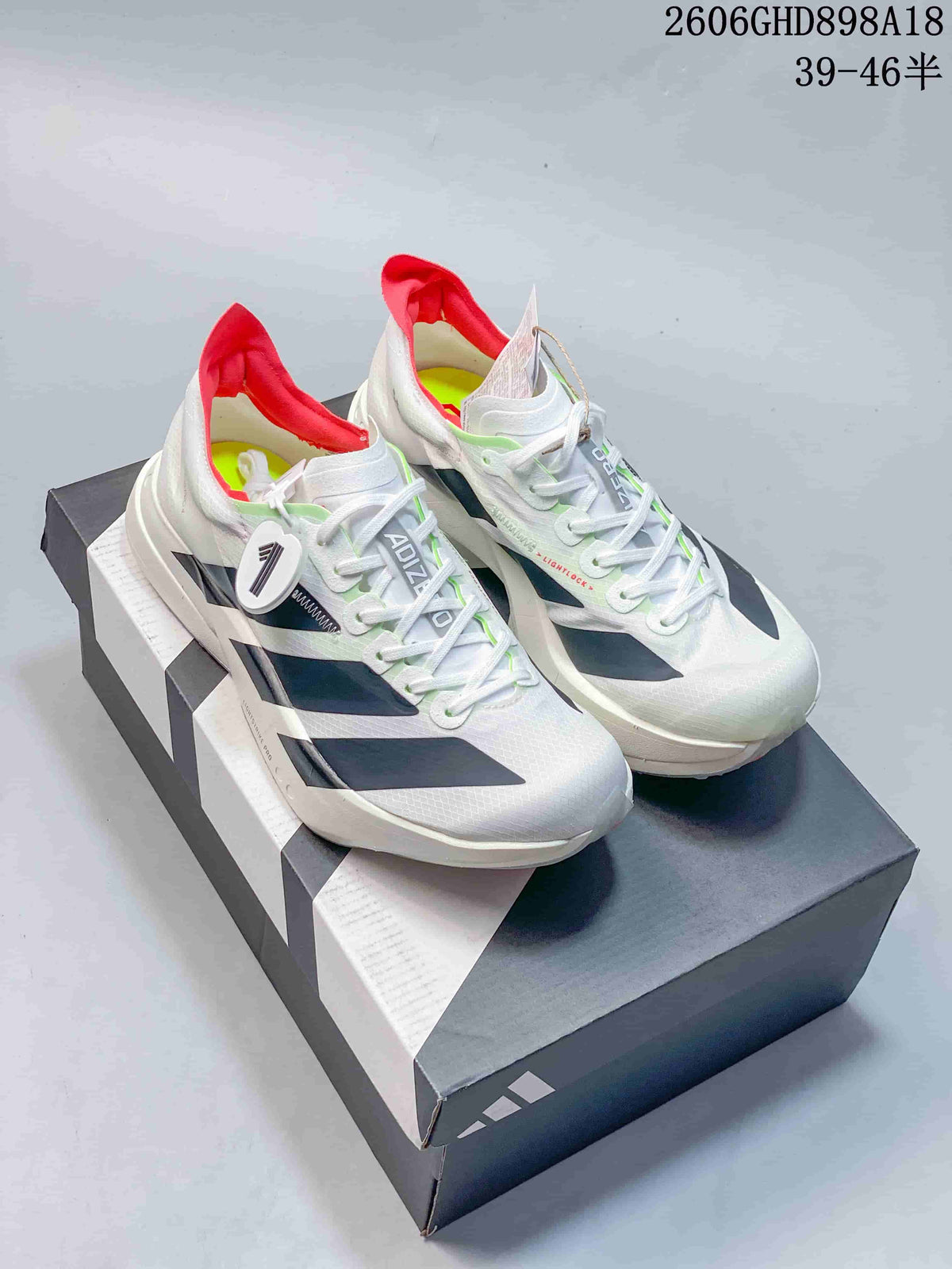 Pair of white Adidas Adizero running shoes with dark stripes and red heel accents on a shoe box.