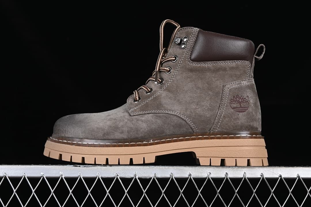 Side view of a gray mid-top boot with brown laces and a tan lugged sole.
