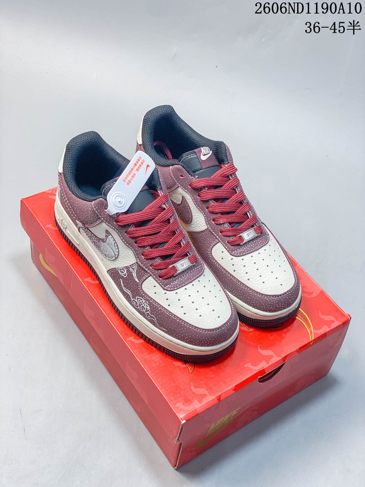 Pair of burgundy and off-white low-top sneakers with red laces and decorative motifs on a red box