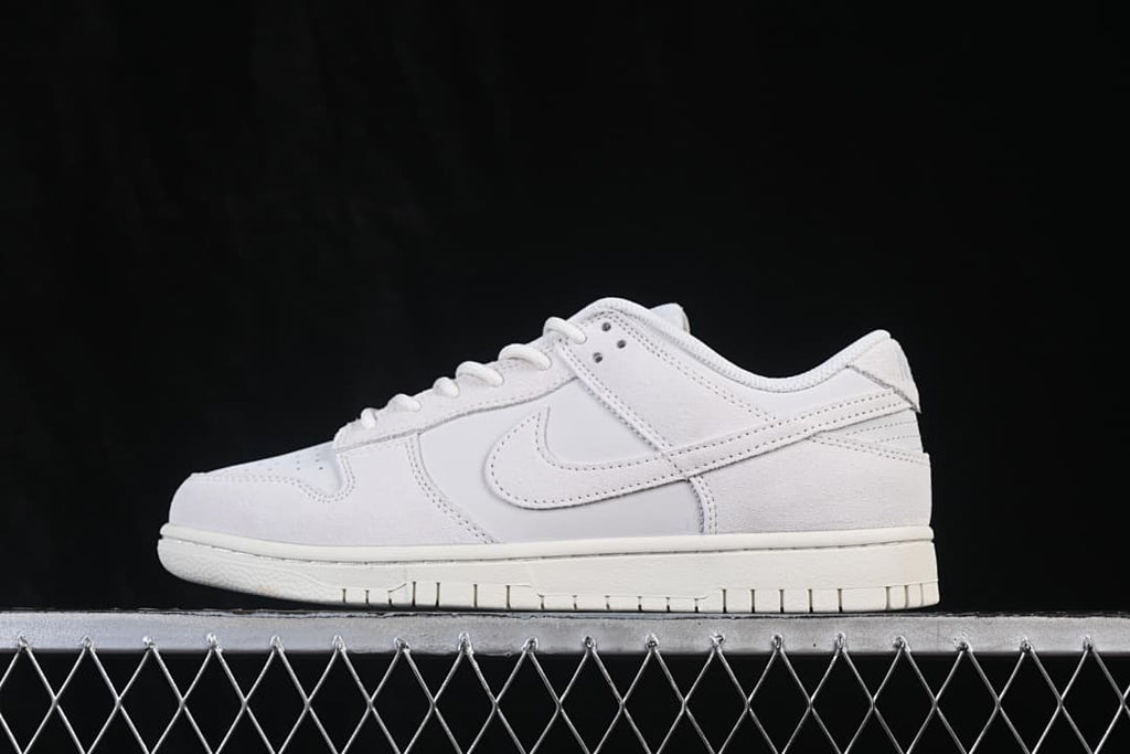 Side view of a white Nike SB Dunk Low sneaker showing its low-top profile, layered panels, tonal Swoosh, and rubber outsole.