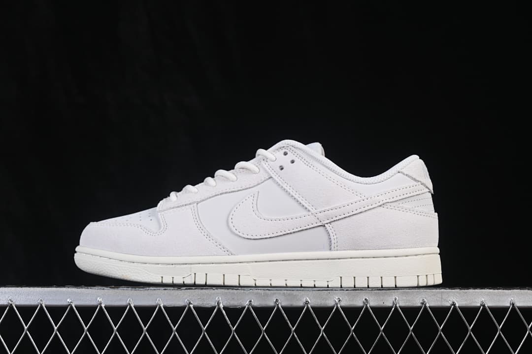Side view of a white Nike SB Dunk Low sneaker showing its low-top profile, layered panels, tonal Swoosh, and rubber outsole.