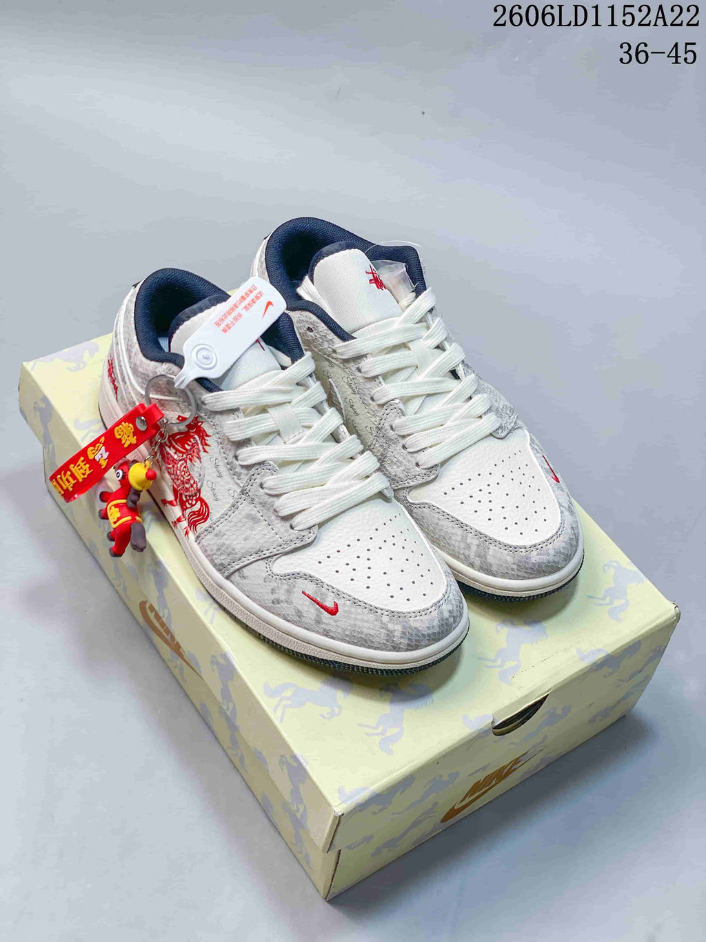 Pair of white and grey Jordan Air Jordan 1 Low sneakers with navy accents and red graphics, shown on a patterned box.