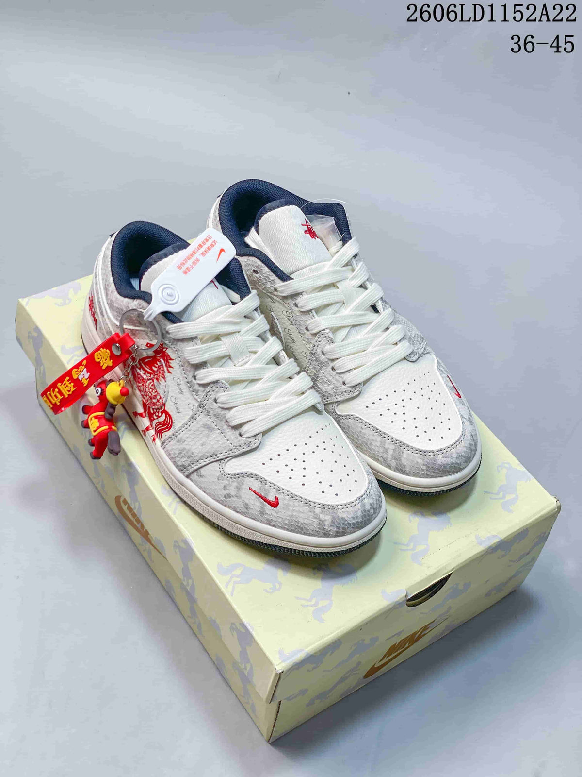 Pair of white and grey Jordan Air Jordan 1 Low sneakers with navy accents and red graphics, shown on a patterned box.