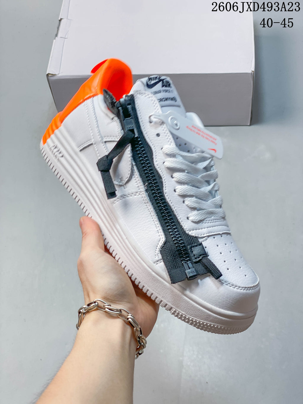 Angled view of the white sneaker with black zipper-style detailing and orange heel