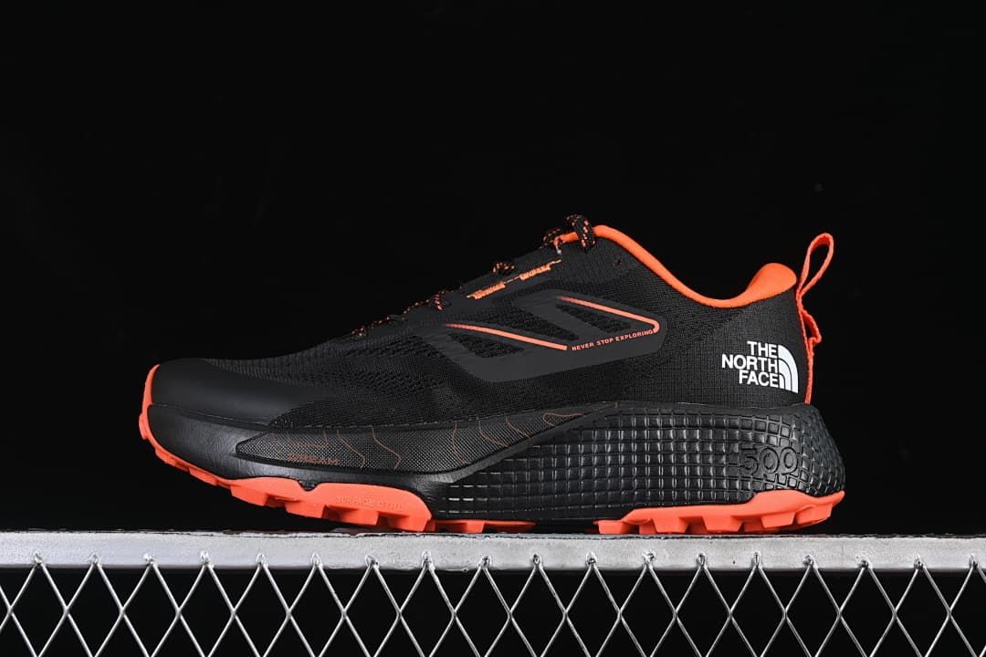 Side view of the black and orange shoe with textured heel and lugged outsole.