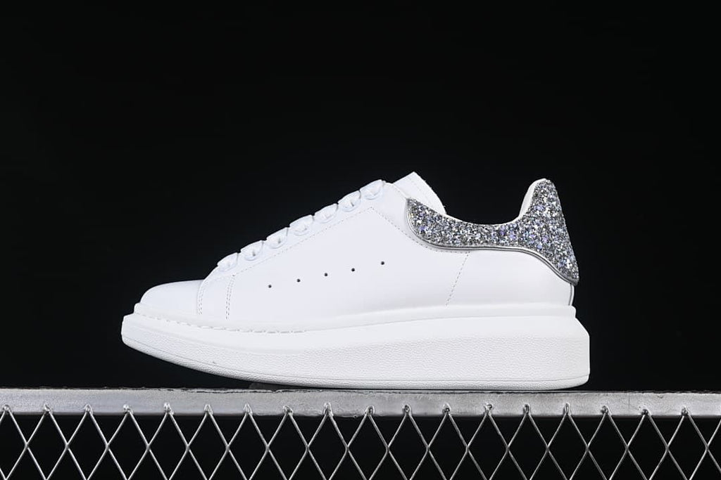 Side profile of a white sneaker with a silver-tone glitter heel panel.