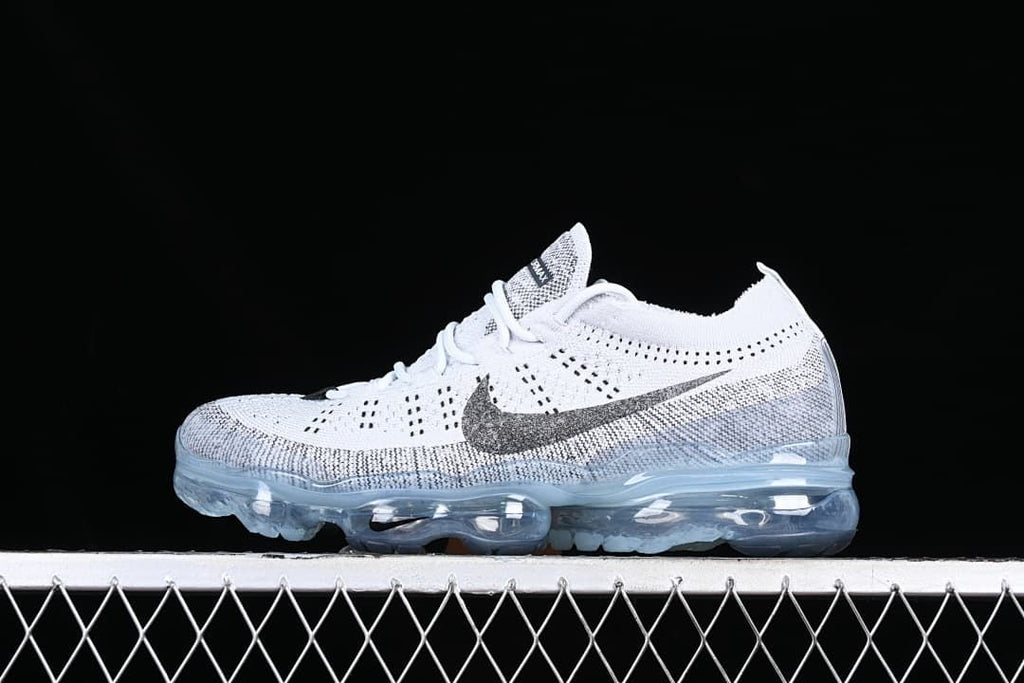 Side view of a white and gray Nike VaporMax Flyknit sneaker with a dark Swoosh and translucent sole.
