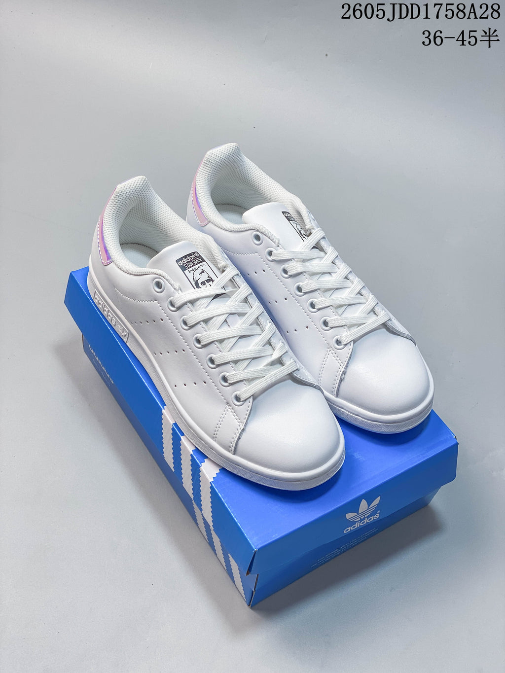 White Adidas Stan Smith-style low-top sneakers with iridescent heel tabs displayed on a blue shoe box