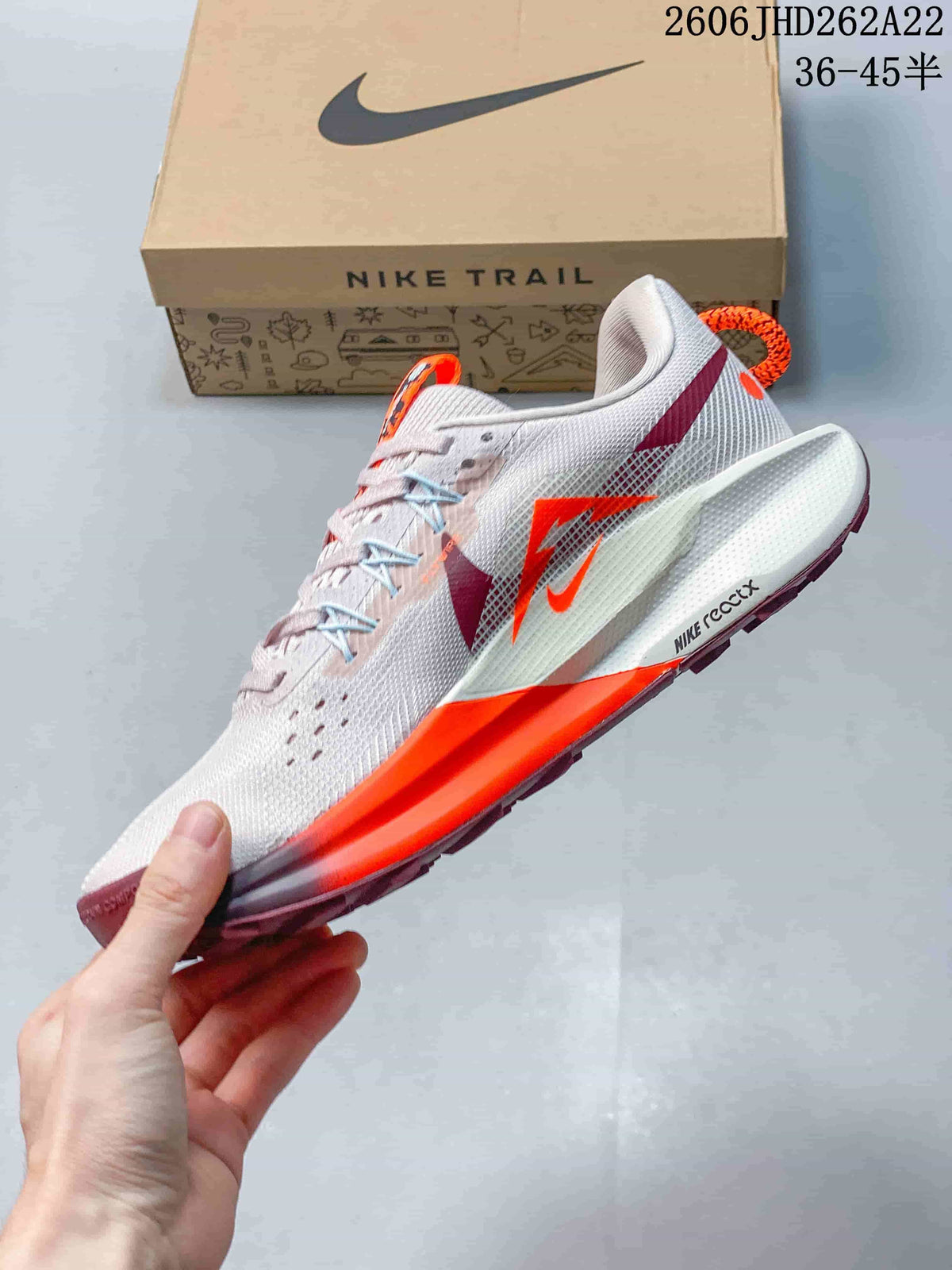 Side view of the Nike Pegasus Trail shoe with pale upper, orange accents, and burgundy details