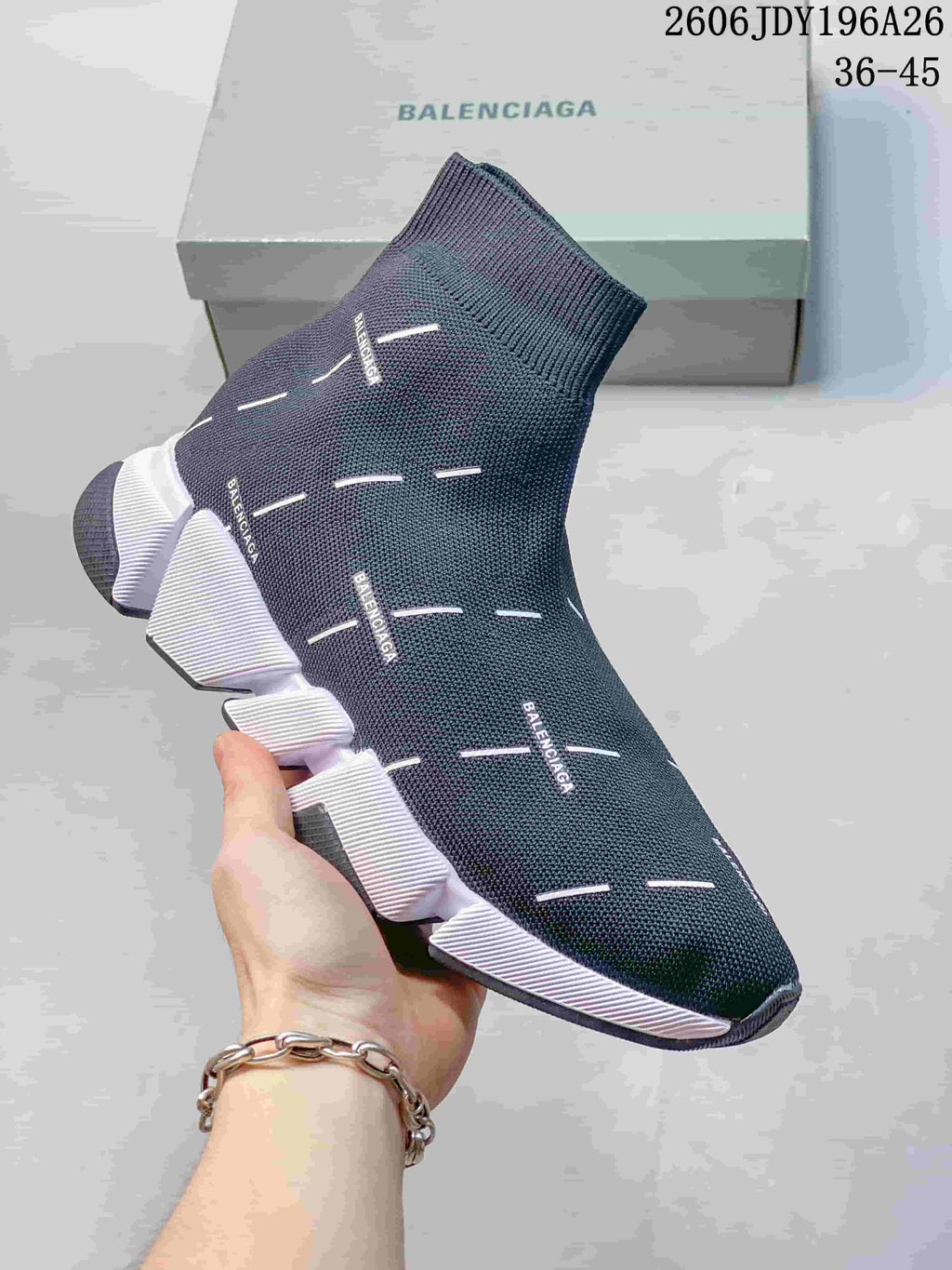 Close view of a dark gray sock-style sneaker with small branding marks and a white segmented sole.