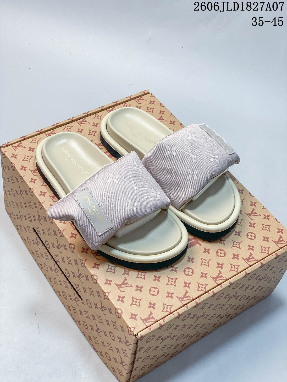 Pair of pale pink monogram-patterned slide sandals on a patterned box