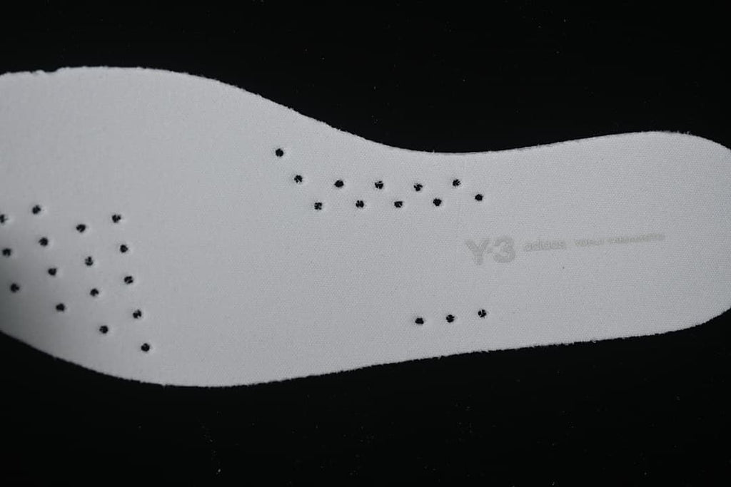 Reverse side of a perforated white shoe insert with faint Y-3 branding