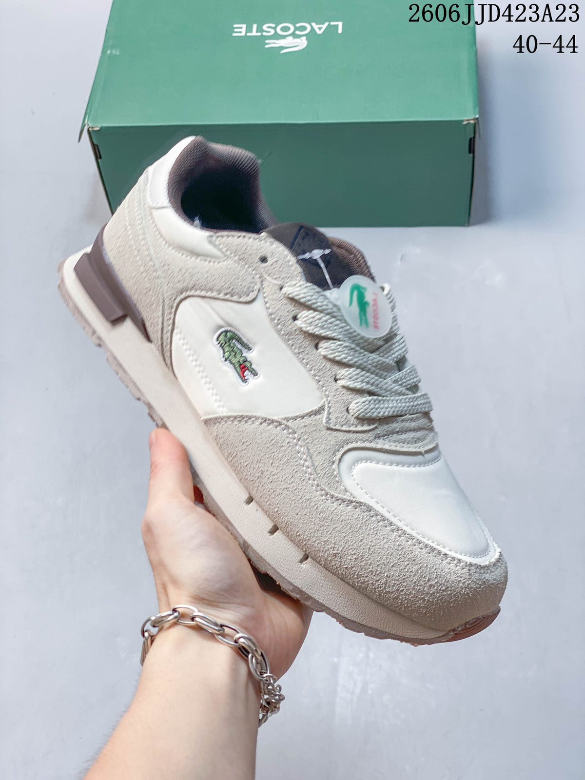 Close view of a cream sneaker with layered panels and a side crocodile emblem