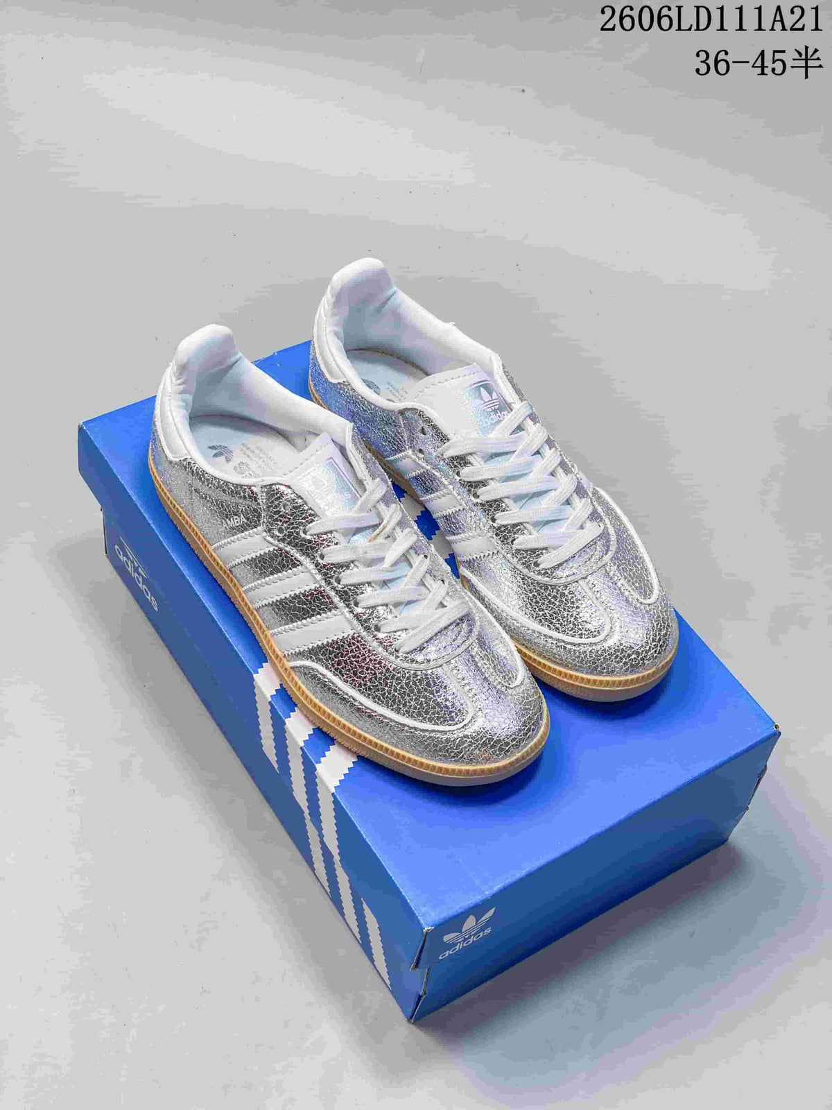 Pair of silver-toned low-top sneakers with white stripes and gum-colored outsoles on a blue box