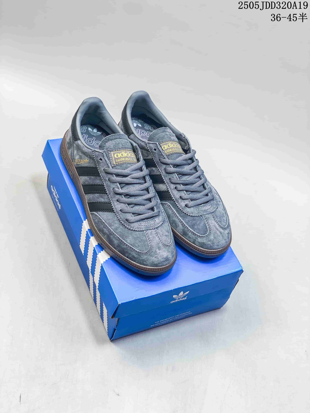 Pair of grey Adidas Gazelle Indoor low-top sneakers with dark stripes and gum-colored soles on a blue shoe box.