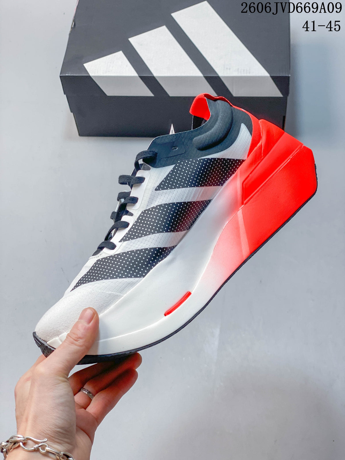 Side view of a white shoe with dark stripes, navy laces, and a bright red heel