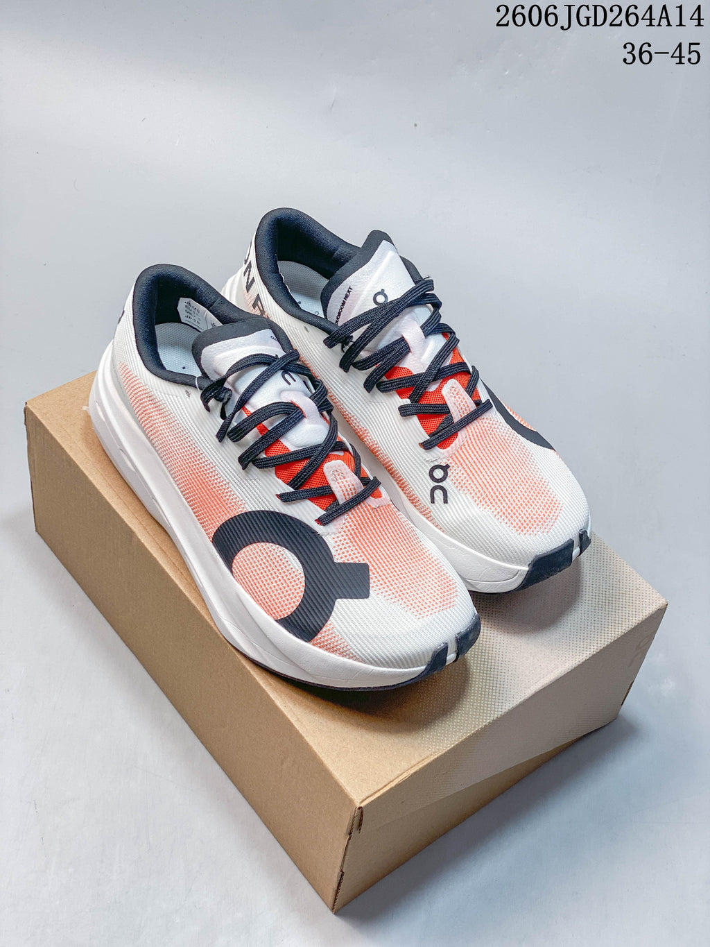 Pair of white and coral On Cloudboom Volt running shoes with dark laces, shown on a box.