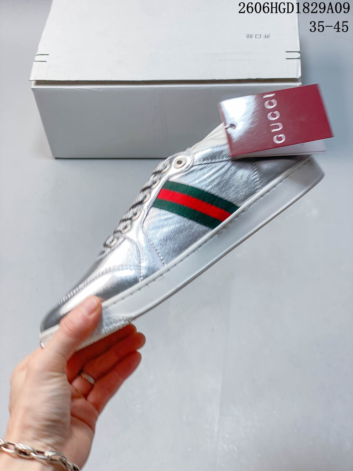 Side profile of a silver sneaker with a green-and-red stripe and a branded hangtag.