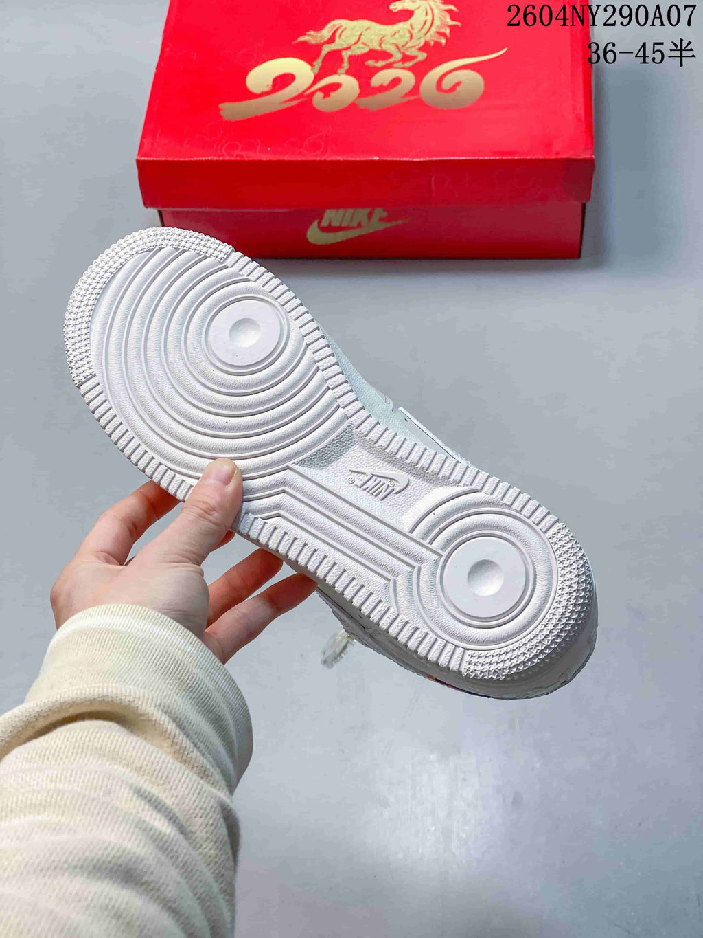 Outsole of a white Nike Air Force 1 sneaker beside a red horse-themed box