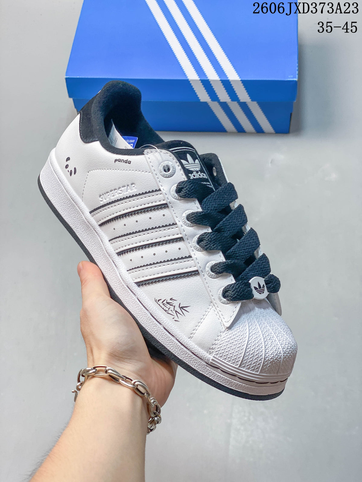 Close side view of a white Superstar sneaker showing dark stripes, shell toe, and panda-inspired heel detail