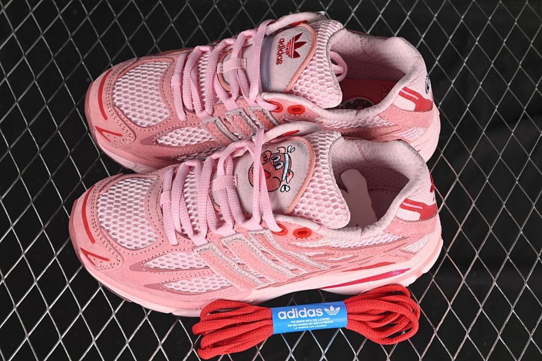 Pair of pink sneakers displayed with an extra set of red laces.