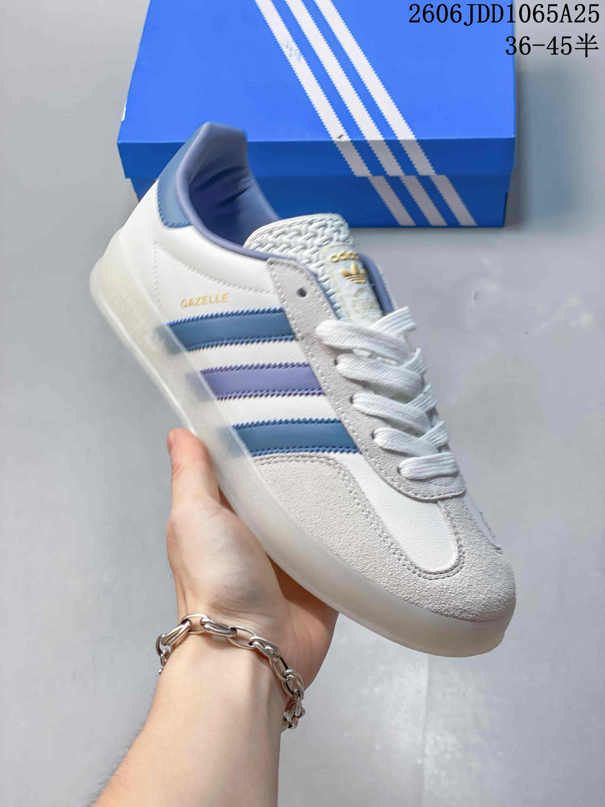 Angled view of a white and light-gray Adidas Gazelle sneaker with blue and lavender stripes.