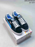 Pair of dark PUMA Suede Shed low-top sneakers with blue side stripes and white laces, shown on a shoe box.
