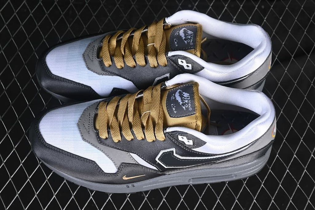 Pair of black, grey, and white Nike Air Max 1 sneakers with gold-tone laces